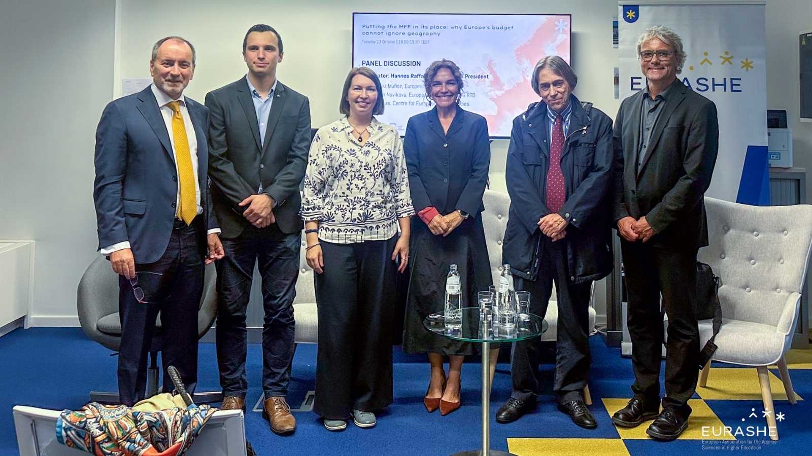 Six people, four men and two women, standing in line next to each other, smiling to the camera